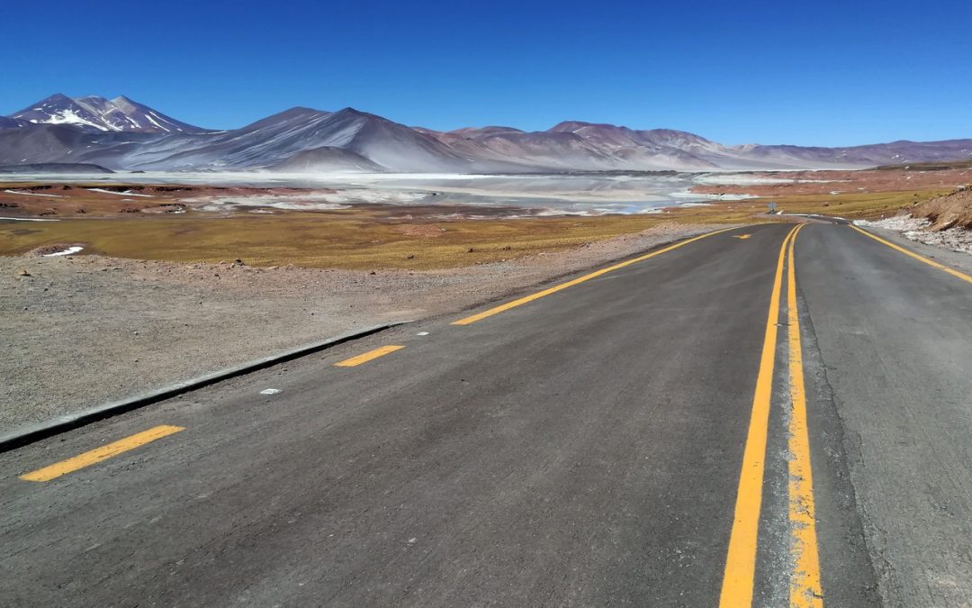 A majestic scene of a paved straight highway going through a snow-capped mountain range on a sunny day